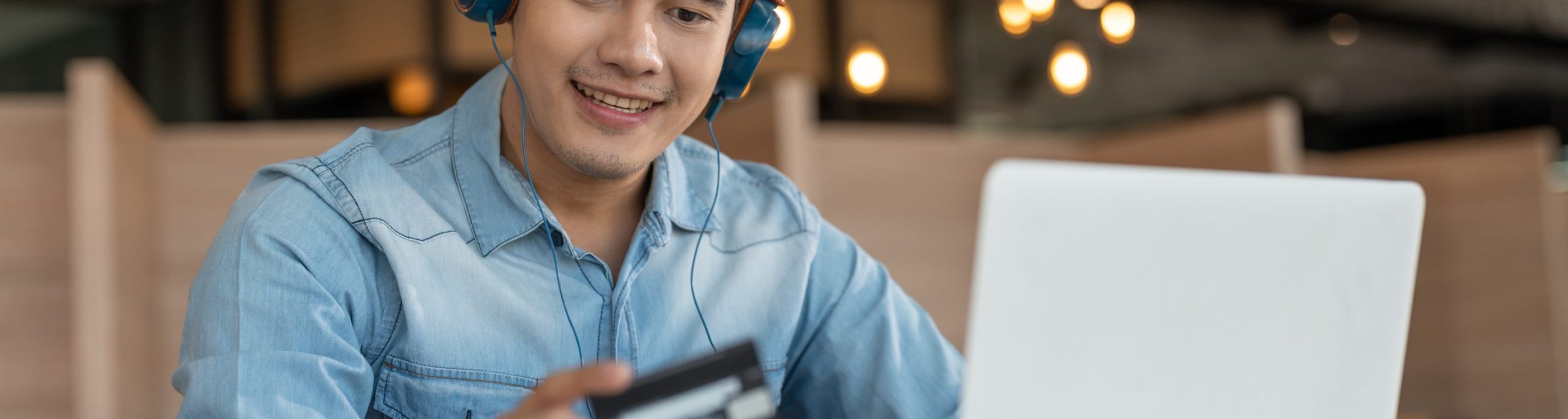Young Asian male in blue shirt using credit card shopping online in laptop. Businessman making payment purchasing on internet.