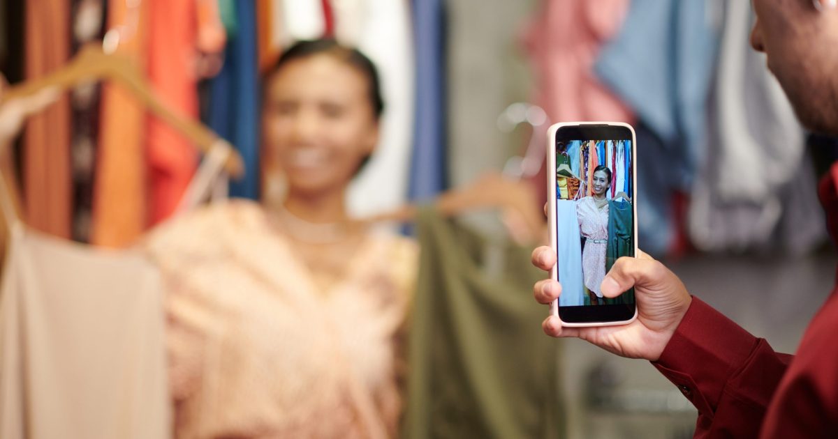 Young man taking photo of friend with dresses for her fashion blog