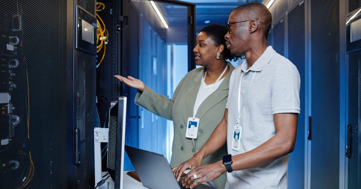Waist up portrait of two IT engineers inspecting server cabinets and setting up internet network