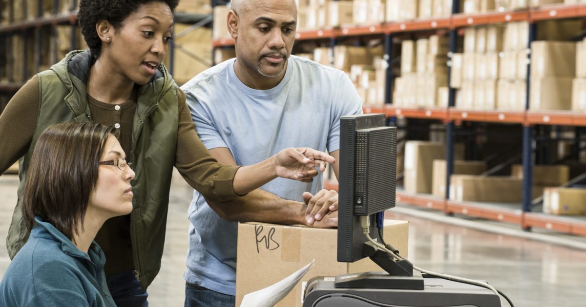 Warehouse workers checking inventory on a computer in a large distrubiton warehouse.