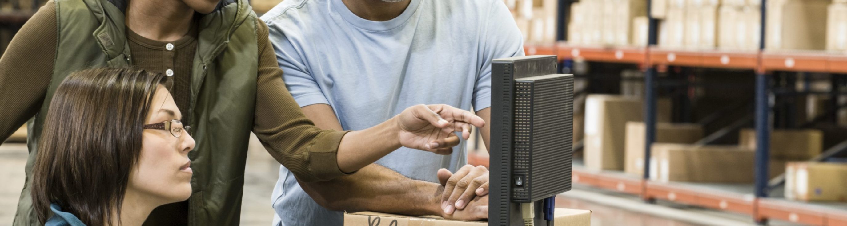 Warehouse workers checking inventory on a computer in a large distrubiton warehouse.